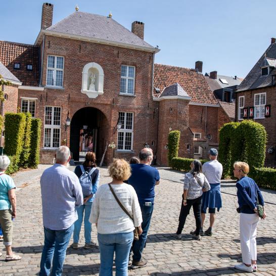Een groepje deelnemers luistert naar een gids tijdens een wandeling op het begijnhof