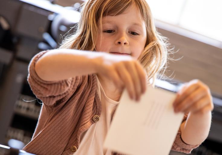 Een kind met een papier aan de drukpers